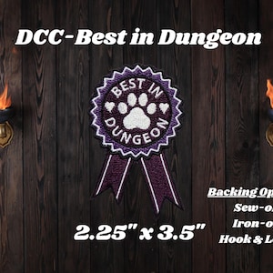 Könnte beinhalten: Ein violett-weißes besticktes Abzeichen in Form einer Auszeichnungsschleife mit Pfotenabdruck und dem Text "BEST IN DUNGEON". Das Abzeichen misst 5,7 cm x 8,9 cm. Der Text darüber lautet "DCC-Best in Dungeon" und darunter stehen Befestigungsoptionen.