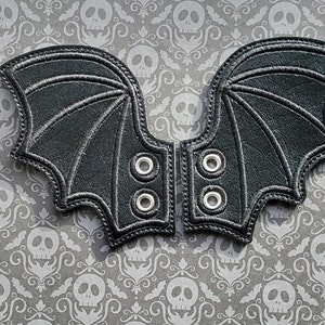 Peut inclure: Une paire de breloques de chaussures en forme d'ailes de chauve-souris en cuir noir avec des œillets argentés. Les breloques sont conçues pour être attachées aux chaussures pour un costume d'Halloween ou un usage quotidien.