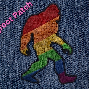 Könnte beinhalten: Ein regenbogenfarbener Bigfoot-Patch, gestickt auf einem blauen Jeansstoff. Der Patch zeigt eine gehende Bigfoot-Silhouette mit einem Farbschema aus Rot, Orange, Gelb, Grün, Blau, Indigo und Violett.