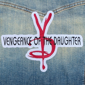 May include: A white embroidered patch with the text "VENGEANCE OF THE DAUGHTER" in black, and a red stylized "YD" design. The patch is sewn onto a denim jacket.