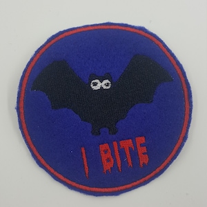 May include: A blue and red embroidered patch featuring a black bat and the text "I BITE" in red.