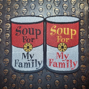 May include: Two red and white soup cans with the text "Soup for My Family" on each. The cans are embroidered on a black background with a skull pattern.