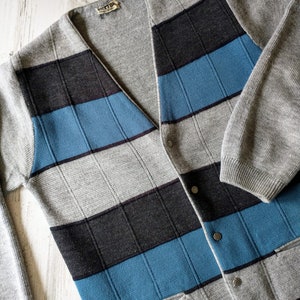 May include: A gray striped cardigan with blue and black stripes. The cardigan has a v-neck and button closure. The label reads "Kurtis" in black text.