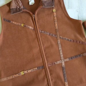 May include: A brown sleeveless vest with a zipper closure and a patterned collar. The vest has decorative brown snakeskin-like trim with gold accents.
