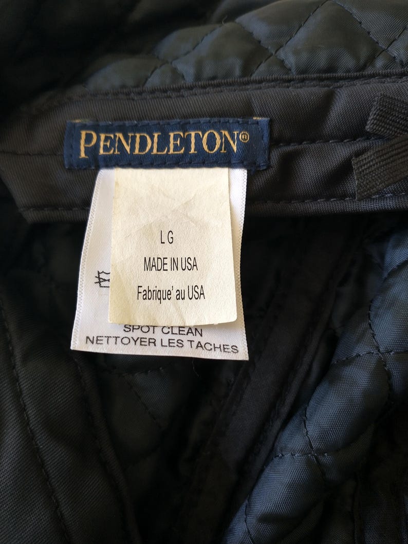 May include: Close-up of a dark gray quilted fabric with a tag. The tag reads "PENDLETON&reg;" in gold lettering. Below the brand name, the tag indicates "LG", "MADE IN USA", and "SPOT CLEAN".
