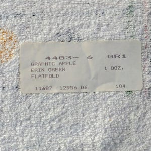 K&ouml;nnte beinhalten: Wei&szlig;es Etikett mit schwarzem Text, der "4483-6 GR1 1 DOZ. 11687 12956 06 104" und "GRAPHIC APPLE ERIN GREEN FLATFOLD" lautet.