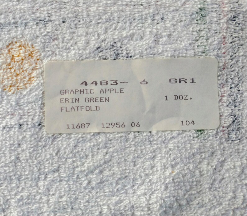 K&ouml;nnte beinhalten: Wei&szlig;es Etikett mit schwarzem Text, der "4483-6 GR1 1 DOZ. 11687 12956 06 104" und "GRAPHIC APPLE ERIN GREEN FLATFOLD" lautet.