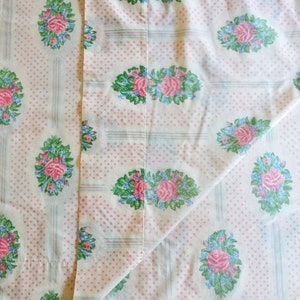 May include: A folded white sheet with a repeating pattern of pink roses, blue accents, and green leaves. The design is set against a backdrop of small pink polka dots and vertical stripes.