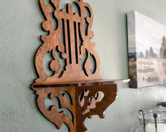 May include: A wooden wall shelf with intricate scrollwork and a corner design. The shelf is stained a dark brown color and has a decorative, ornate style.