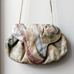 May include: A vintage leather shoulder bag with a unique abstract design in shades of brown, pink, and green. The bag has a flap closure and a long strap.