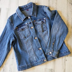 May include: A white ceramic mug with a black handle and the text "But First, Coffee" in a bold, black font. The mug is set against a blurred background, suggesting a cozy setting.