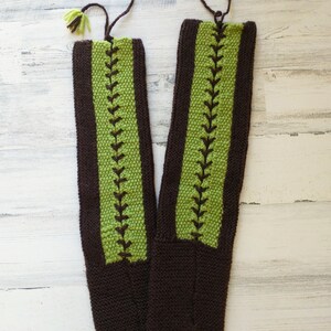 May include: A pair of brown and green knitted slipper socks with green tassels. The socks have a brown and green striped pattern with a green leaf design.