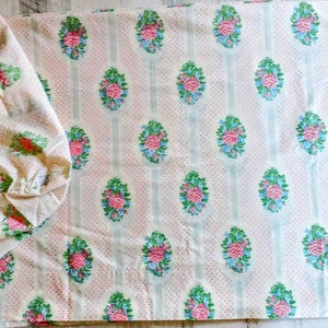 May include: A flat sheet and pillowcase set with a floral pattern. The fabric is a light beige with a repeating design of pink roses, blue accents, and green leaves. The background has a dotted pattern and vertical stripes.