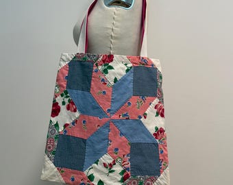 May include: A quilted tote bag with a starburst design. The bag features a patchwork of pink, blue, and floral fabric. White straps and a pink trim complete the design. The bag is displayed on a mannequin.