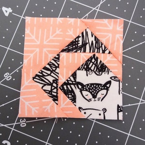 May include: A pink and black fabric square with a geometric pattern. The center of the square features a white fabric with a black and white illustration of a fox.
