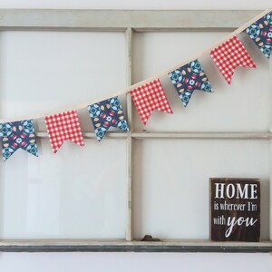 May include: A red and blue fabric banner with a white background hangs in front of a window. The banner has a repeating pattern of geometric shapes. Below the banner is a wooden sign with the text "HOME is wherever I'm with you".