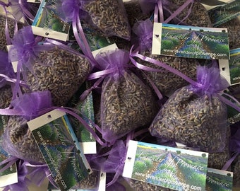 May include: A close-up of multiple small purple mesh bags filled with dried lavender buds. Each bag has a white tag attached with the text "Lavender of Provence" and the website address "www.lavenderofprovence.com".