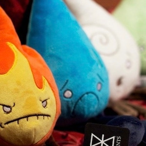 A group photo that shows all 4 elements (fire, water, air and earth) with the fire elemental plush toy in the front and in focus. The other three are blurry to keep the focus on the fire plushie. It has a angry face.