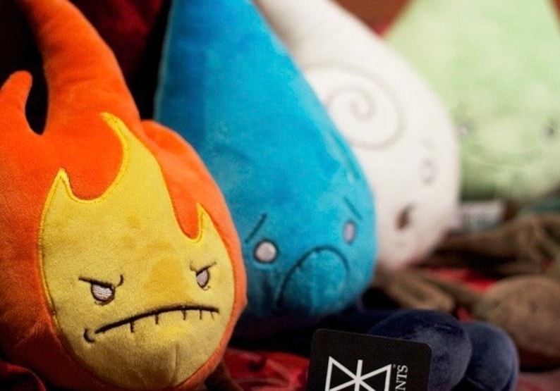 A group photo that shows all 4 elements (fire, water, air and earth) with the fire elemental plush toy in the front and in focus. The other three are blurry to keep the focus on the fire plushie. It has a angry face.