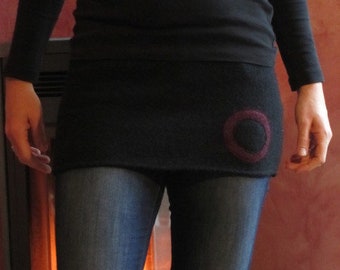 May include: A black long-sleeved shirt with a black skirt and a circle design on the skirt. The person is wearing blue jeans.