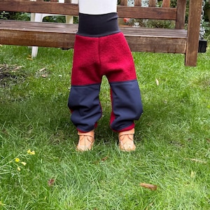 Può includere: Pantaloni da bambino rossi e blu navy con fascia in vita nera. I pantaloni sono realizzati in un materiale morbido e sono progettati per il comfort. I pantaloni sono mostrati su un bambino in piedi sull'erba verde.