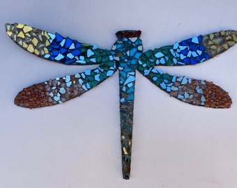 May include: A mosaic dragonfly with blue, green, and brown glass pieces. The dragonfly's wings are spread out and its body is long and thin.
