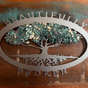May include: A silver metal tree with a mirrored, broken glass design. The tree is surrounded by an oval frame with the words "Beautifully Broken" inscribed around it.
