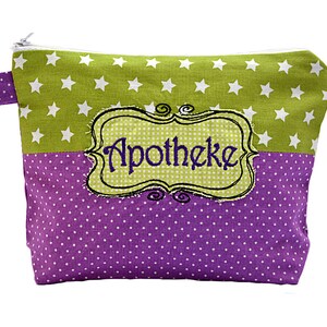Puede incluir: Una bolsa con cremallera con un diseño de bloques de color. La mitad superior es verde lima con estrellas blancas, y la mitad inferior es morada con lunares blancos. La palabra "Apotheke" está bordada en verde dentro de un marco decorativo.