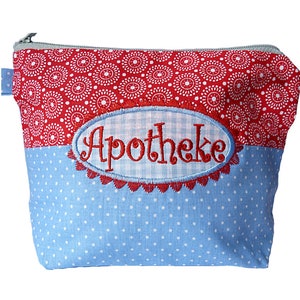 Puede incluir: Bolsa de cosméticos con cremallera, con un estampado floral rojo y blanco en la parte superior y lunares azules en la inferior. La bolsa presenta un óvalo bordado con la palabra "Apotheke" en letras rojas.
