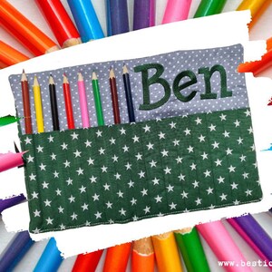 Könnte beinhalten: Ein grüner Stoff-Bleistiftetui mit weißen Sternen und einer grauen Stoffklappe mit dem Namen "Ben" bestickt.