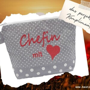 Könnte beinhalten: Graue Kosmetiktasche mit weißen Punkten, mit dem rot gestickten Wort "Chefin", einem roten Herz und dem Wort "mit". Eine kleine Notiz lautet "das perfekte Kompliment".