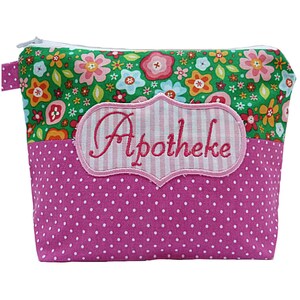 Puede incluir: Una bolsa con cremallera con estampado floral con una base de lunares rosas y una parte superior floral verde. La bolsa tiene una etiqueta a rayas rosas y blancas con la palabra "Apotheke" bordada en rosa.