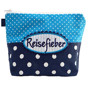 Puede incluir: Una bolsa con cremallera de lunares azules y marino con la palabra "Reisefieber" bordada en la parte delantera. La bolsa tiene una cremallera blanca y una pequeña etiqueta azul en el lateral. La sección superior es azul claro con lunares blancos, y la inferior es azul marino con lunares blancos.
