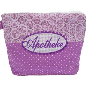 Puede incluir: Pequeño neceser rectangular morado con cremallera blanca. La bolsa presenta un estampado de lunares en la mitad inferior y un diseño floral en la mitad superior. Un parche ovalado bordado con la palabra "Apotheke" está centrado en la parte delantera.