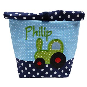 May include: A blue and white polka-dot fabric storage bin with a green tractor applique and the name "Philip" embroidered in green. The top and bottom borders are navy blue with white polka dots.