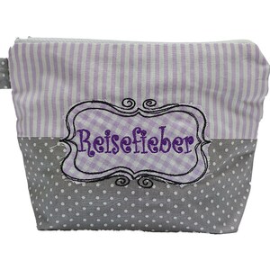 May include: A small, rectangular cosmetic bag with a zip closure. The top half has vertical lavender and white stripes, while the bottom half is grey with white polka dots. A lavender gingham patch with the word "Reisefieber" in purple script is sewn on the front.
