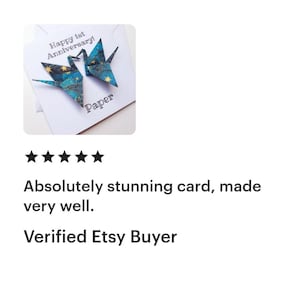 K&ouml;nnte beinhalten: Eine wei&szlig;e Karte mit dem Text "Happy 1st Anniversary!" und dem Wort "Paper". Zwei Origami-Kraniche mit blau-goldenen Mustern befinden sich auf der Karte. Die Karte hat eine F&uuml;nf-Sterne-Bewertung.