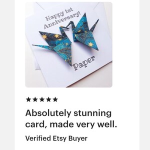 K&ouml;nnte beinhalten: Eine wei&szlig;e Karte mit zwei Origami-Kranichen in Blau- und Goldt&ouml;nen, mit dem Text "Happy 1st Anniversary!" und "Paper". Die Karte ist handgefertigt.