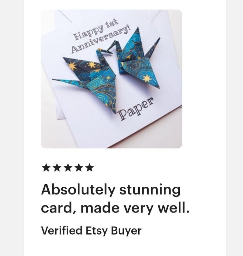 K&ouml;nnte beinhalten: Eine wei&szlig;e Karte mit zwei Origami-Kranichen in Blau- und Goldt&ouml;nen, mit dem Text "Happy 1st Anniversary!" und "Paper". Die Karte ist handgefertigt.