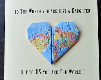 May include: A greeting card with the message "TO THE WORLD YOU ARE JUST A DAUGHTER BUT TO US YOU ARE THE WORLD!" features a blue origami heart made from a world map. The card is cream-colored.