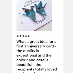 K&ouml;nnte beinhalten: Eine wei&szlig;e Karte mit zwei Origami-Kranichen in Blau- und Goldt&ouml;nen, mit dem Text "Happy 1st Anniversary!" und "Paper". Die Kraniche sind aus gemustertem Papier gefaltet. Ein sch&ouml;nes Geschenk zum ersten Jahrestag.