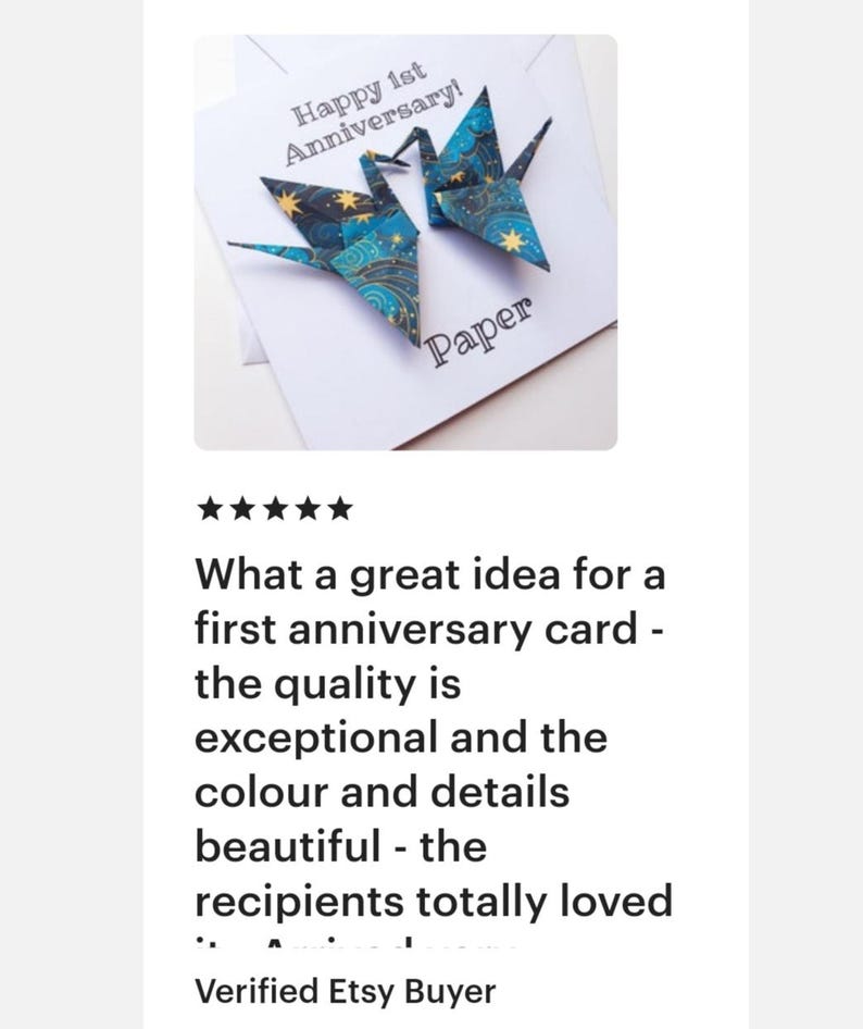 K&ouml;nnte beinhalten: Eine wei&szlig;e Karte mit zwei Origami-Kranichen in Blau- und Goldt&ouml;nen, mit dem Text "Happy 1st Anniversary!" und "Paper". Die Kraniche sind aus gemustertem Papier gefaltet. Ein sch&ouml;nes Geschenk zum ersten Jahrestag.