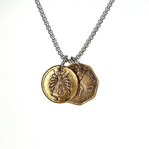 May include: A silver chain necklace featuring two bronze pendants. One is a round pendant with a religious figure, the other an octagonal coin with a kangaroo image. The pendants are attached to the chain with small silver rings.
