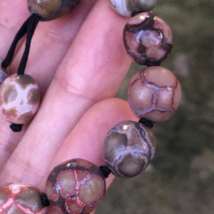 Op de afbeelding: Een armband gemaakt van bruine, witte en rode agaat kralen met een zwart koord.