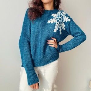 May include: A teal blue knitted sweater with a white snowflake design on the shoulder.