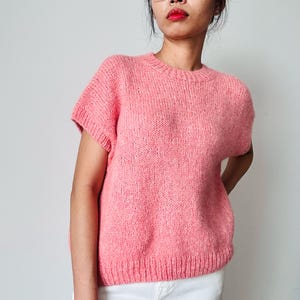 May include: A pink knitted sweater with short sleeves and a round neckline.