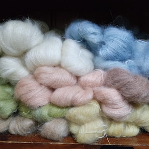 May include: A collection of fluffy yarn in various colors, including white, light blue, pink, green, and brown. The yarn is arranged in a pile, suggesting a craft supply for knitting or crocheting projects.