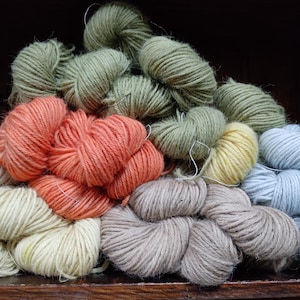 Può includere: Una collezione di gomitoli di filato colorati in varie tonalità, tra cui arancione, verde, giallo e blu. Il filato è disposto in un mucchio, suggerendo un progetto artigianale o di maglieria. L'immagine mostra la consistenza e le variazioni di colore del filato.