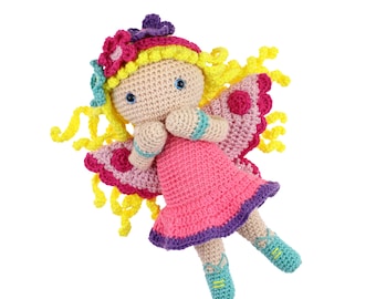 Puede incluir: Una muñeca de hada de crochet con alas rosas y moradas, cabello amarillo y un vestido rosa. La muñeca lleva zapatos azules y amarillos.