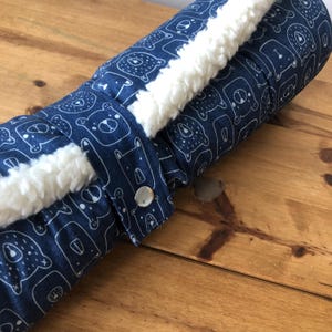 May include: A blue and white patterned fabric roll with a white sherpa lining. The fabric features a repeating pattern of white bears on a dark blue background.